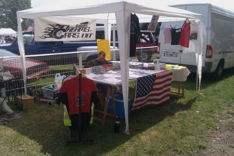 1991 Ford Crown Victoria - A vendor displays merchandise, including t-shirts and license plates, under a tent at an outdoor event.