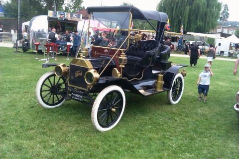 1991 Ford Crown Victoria - This antique Ford Model T touring car is parked on a grassy field with people and a food truck in the background.
