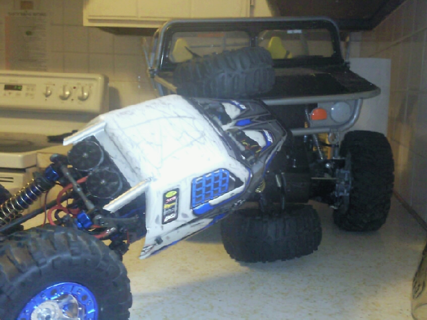 Two remote control rock crawler vehicles, one white and blue, the other black, on a counter
