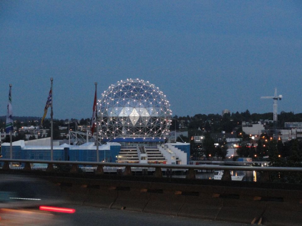 Geodesic dome stadium at dusk with city skyline and crane
