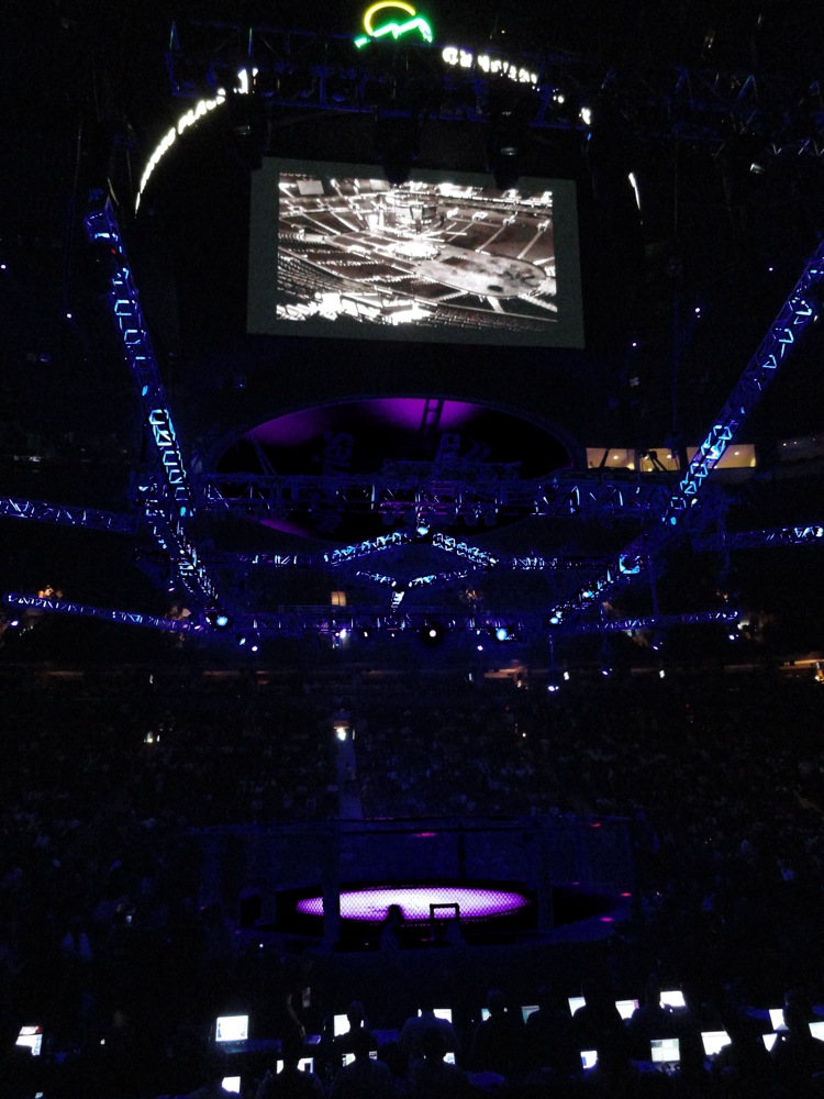 Arena with a large screen showing a map, lights, and a crowd