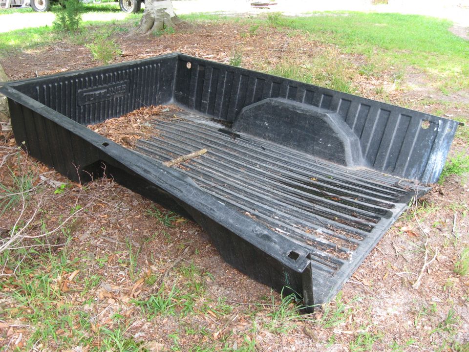 Black drop-in plastic pickup bed liner with Tuff Liner logo lying in a grassy yard