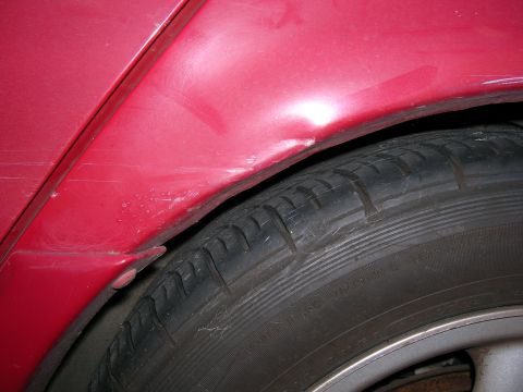 1993 Ford Taurus - A dent is visible on the red rear fender of a 1993 Ford Taurus, just above the tire.