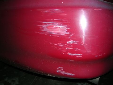 1993 Ford Taurus - Close-up of a red car's bumper showing significant damage from scratches and impacts.