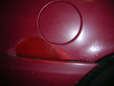 1993 Ford Taurus - Close-up of a red car's rear quarter panel showing the fuel filler door and a portion of the taillight.