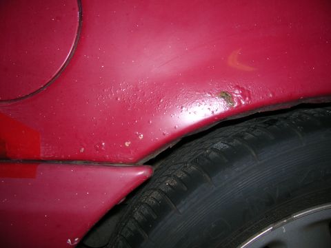1993 Ford Taurus - Rust is forming on the fender of this red vehicle, indicating potential body damage.