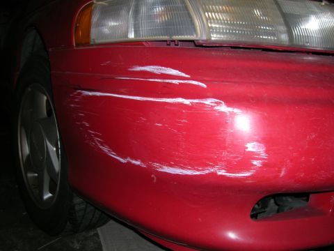 1993 Ford Taurus - Front bumper of a red 1993 Ford Taurus shows significant white paint transfer and numerous scratches.