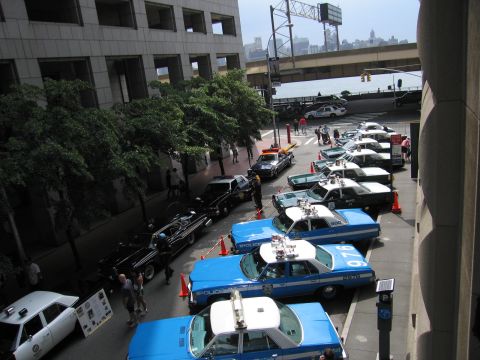 1991 Ford LTD Crown Victoria - Overhead view of blue-and-white NYPD sedans angle-parked along a downtown street near an elevated roadway and waterfront.