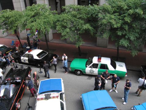 1991 Ford LTD Crown Victoria - Elevated view of a green-and-white police station wagon and a black-and-white cruiser with officers and spectators on a tree-lined street.