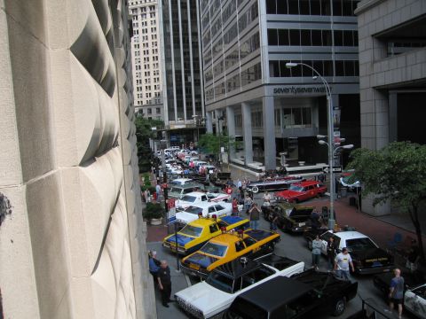 1991 Ford LTD Crown Victoria - View down a downtown street between tall buildings, lined with vintage cars, yellow taxis and crowds at a car display.