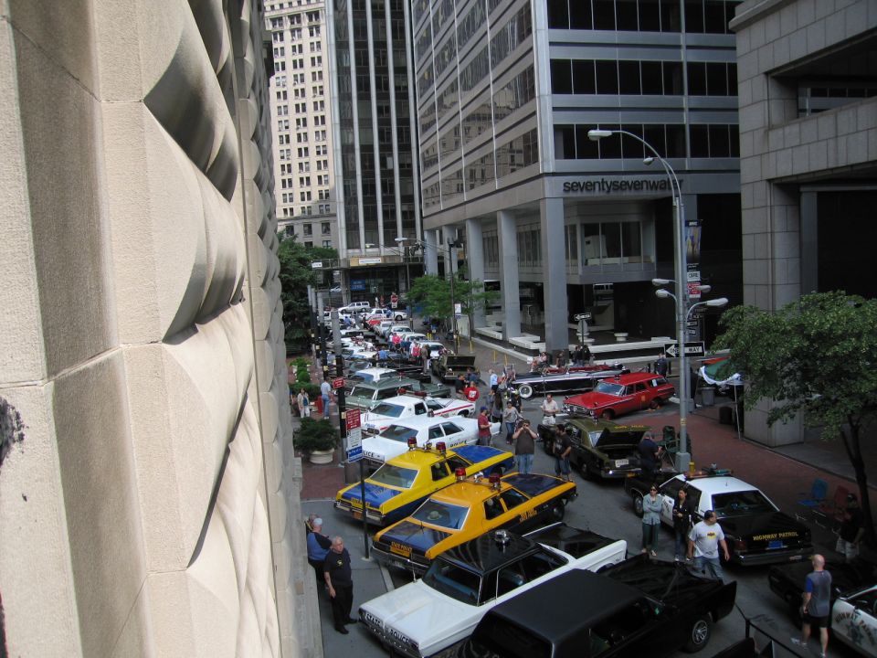 High view down a city street lined with vintage cars and yellow taxis