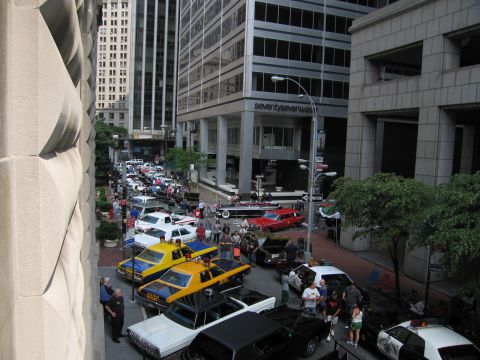 1991 Ford LTD Crown Victoria - Elevated view of a packed downtown street display with yellow taxis, a red sedan and a large crowd between office towers.