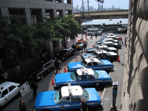 1991 Ford LTD Crown Victoria - Elevated view of blue-and-white NYPD sedans angle-parked along a downtown street near an overpass and waterfront skyline.
