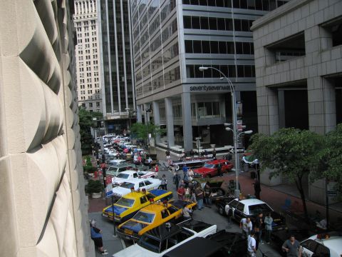 1991 Ford LTD Crown Victoria - Elevated view down a downtown street lined with vintage cars, yellow taxis and pedestrians between tall office buildings.
