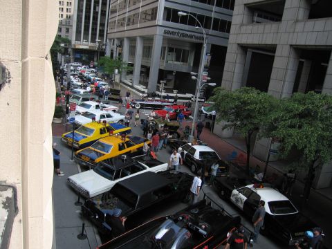 1991 Ford LTD Crown Victoria - Elevated view of a crowded downtown street car show with yellow taxis, vintage police cars and many spectators between buildings.