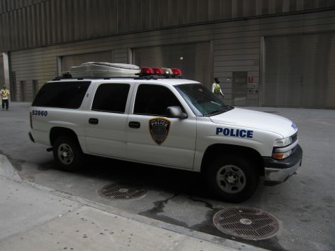 1991 Ford LTD Crown Victoria - white Chevrolet Suburban police SUV numbered 53960 with a roof cargo box and light bar is parked beside a gray building.