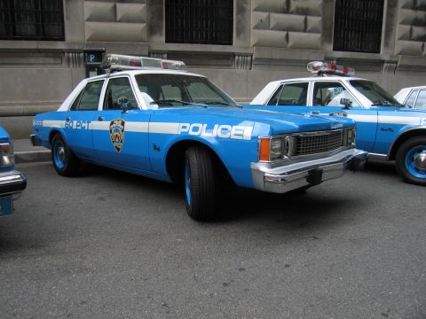 1991 Ford LTD Crown Victoria - vintage light-blue-and-white NYPD POLICE sedan with a roof light bar sits parked among other matching cruisers on a street.