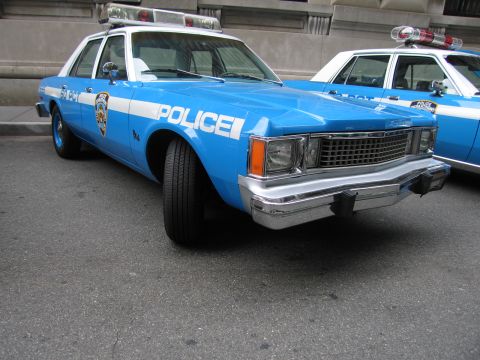 1991 Ford LTD Crown Victoria - front of a vintage light-blue-and-white NYPD POLICE sedan shows a chrome grille and bumper, with a similar cruiser beside it.
