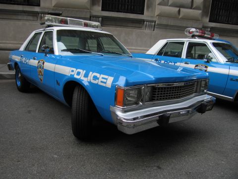 1991 Ford LTD Crown Victoria - vintage light-blue-and-white NYPD POLICE sedan with chrome bumper and roof light bar is parked at the front of a row of cruisers.