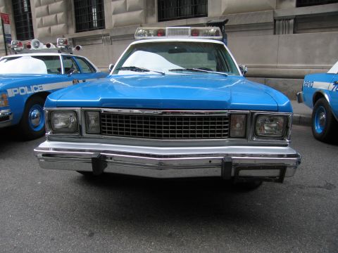 1991 Ford LTD Crown Victoria - head-on front of a vintage blue police sedan shows dual headlights, a chrome grille and bumper, flanked by other blue cruisers.