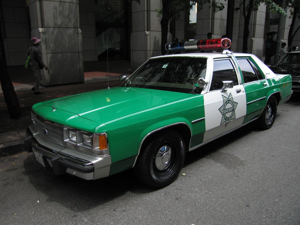 Green and white Sheriff sedan, front quarter, parked curbside