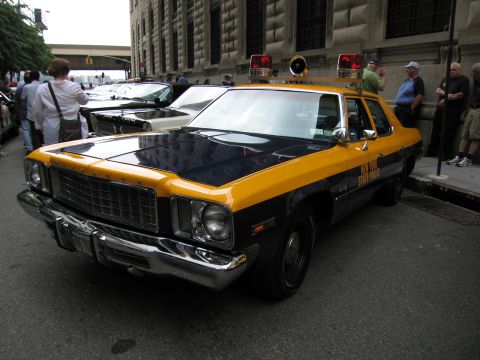 1991 Ford LTD Crown Victoria - yellow-and-black State Police sedan with roof dome lights and a chrome grille is parked on a street as onlookers stand nearby.