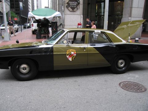 1991 Ford LTD Crown Victoria - black-and-tan sedan with a Maryland state crest on the door is parked in profile on a street near a Financial Square building.