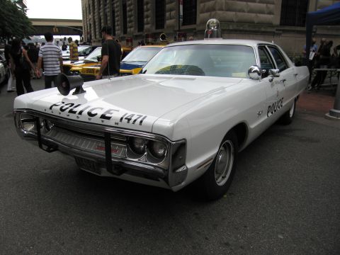 1991 Ford LTD Crown Victoria - white vintage sedan marked POLICE 1471 with a chrome push bar and roof light sits on a street near other parked cruisers.