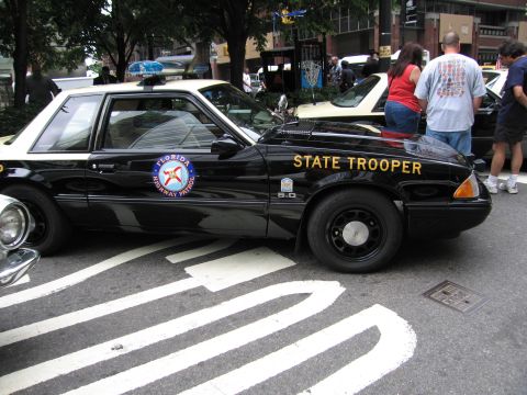 1991 Ford LTD Crown Victoria - black Ford Mustang painted as a Florida Highway Patrol State Trooper car sits at a curbside police-vehicle show.