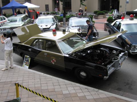 1991 Ford LTD Crown Victoria - black-and-tan vintage police sedan shown with its hood and trunk open on a brick plaza, an emblem on its door.