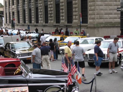 1991 Ford LTD Crown Victoria - dense crowd examines a street lined with classic police and civilian cars, small American flags on a roped-off display car.