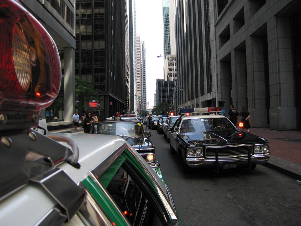 Convoy of classic police cars with lit beacons in a downtown street canyon