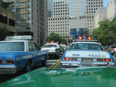 1991 Ford LTD Crown Victoria - Blue-and-white POLICE sedans numbered 9559 and others sit at a downtown intersection lined with high-rise buildings.