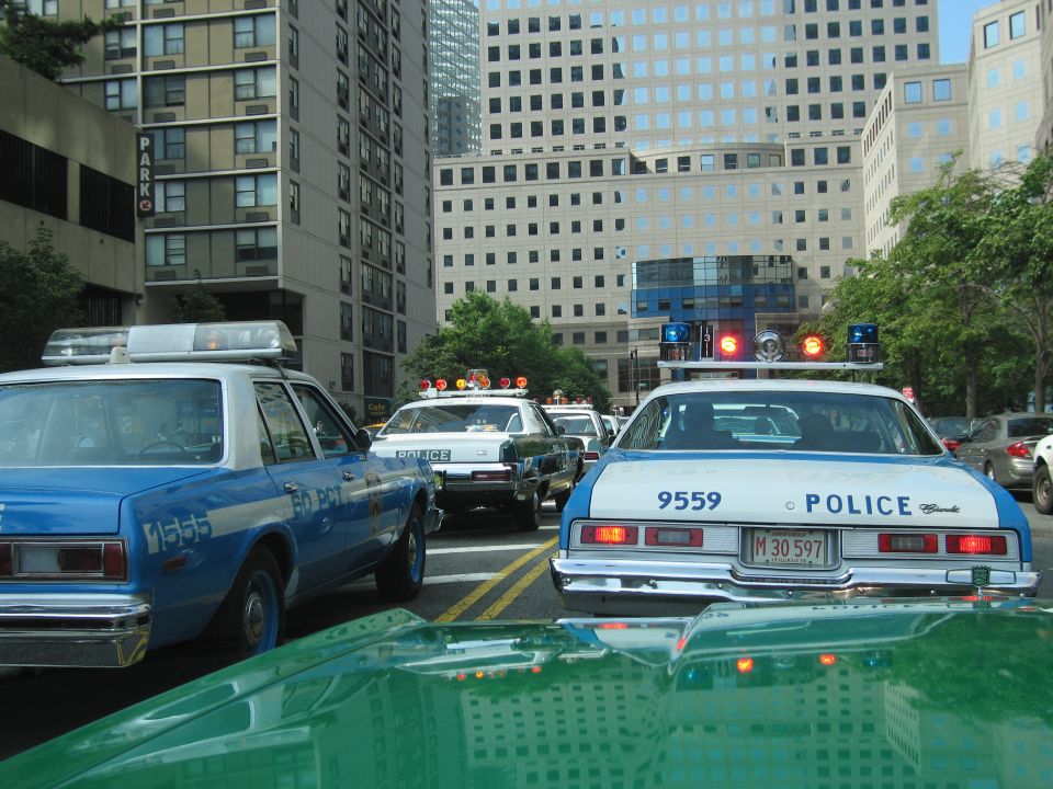 Blue and white NYPD-style police cars stopped on a downtown avenue