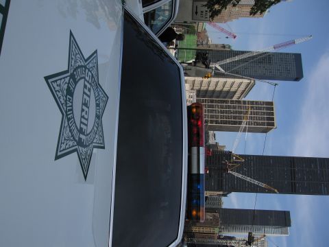 1991 Ford LTD Crown Victoria - white sheriff car's hood displays a County of California seven-point star emblem, with skyscrapers and cranes behind.