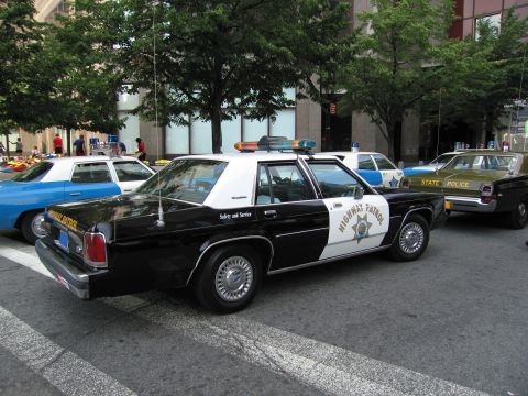 1991 Ford LTD Crown Victoria - black-and-white Highway Patrol sedan with a star badge sits parked among other vintage police cars, including a State Police car, on a city…