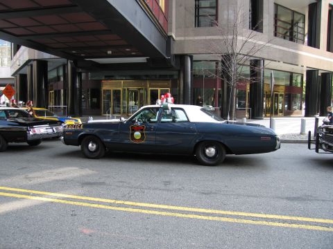 1991 Ford LTD Crown Victoria - dark blue vintage Police sedan with a shield emblem and roof lights parked on a city street, with other classic patrol cars behind it.