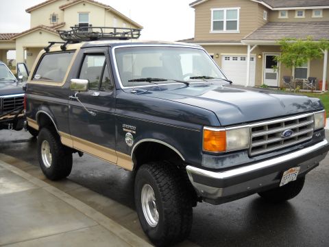 1986 Ford Bronco - This Ford Bronco features a roof rack and two-tone paint, parked in front of a residential house.