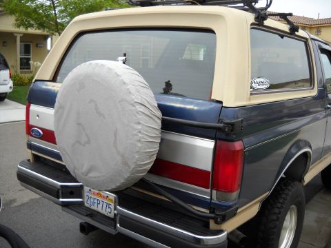 1986 Ford Bronco - Rear view of a blue and tan Ford Bronco, showing its spare tire cover and California license plate.