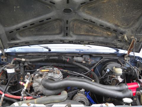 1986 Ford Bronco - The engine bay of a vehicle, showing various hoses, wires, and engine parts under the open hood.