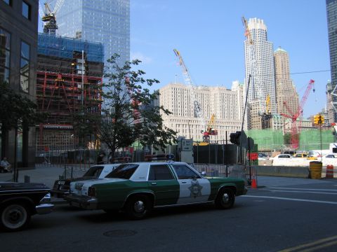 1991 Ford LTD Crown Victoria - green-and-white Sheriff patrol sedan with roof light bar parked along a sidewalk facing a large construction site with cranes and scaffoldi…