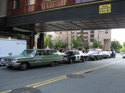 1991 Ford LTD Crown Victoria - row of classic patrol cars led by a green Stratford Police radio-patrol station wagon parked beneath a building overpass marked max height…