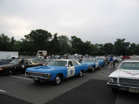 1991 Ford LTD Crown Victoria - blue-and-white vintage police sedan with a star door emblem parked in a row of classic cruisers under an overcast sky.