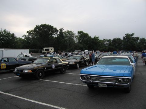 1991 Ford LTD Crown Victoria - black State Trooper Mustang and a blue classic sedan parked among other vintage police cars at an overcast outdoor gathering.