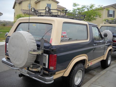 1986 Ford Bronco - Rear view of a 1986 Ford Bronco, equipped with a roof rack and external spare tire mount. Another Bronco is partially visible.