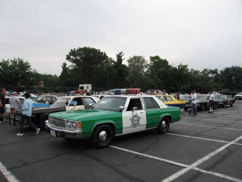 1991 Ford LTD Crown Victoria - green-and-white Ford LTD-style sheriff sedan with a star shield parked among other classic police cars under a gray sky.