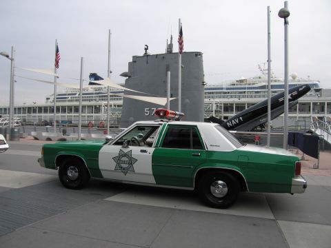 1991 Ford LTD Crown Victoria - Front-quarter view of a green-and-white sheriff sedan with a red roof beacon parked before a museum submarine and Navy anchor.