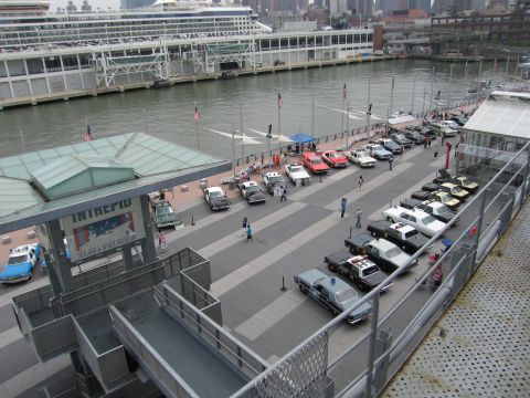 1991 Ford LTD Crown Victoria - Aerial view of vintage cars and police cruisers lined up along a waterfront pier at the Intrepid museum beside a docked cruise ship.