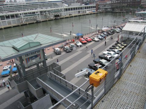 1991 Ford LTD Crown Victoria - Aerial view of classic cars and police cars arranged on a pier with Intrepid signage and a yellow rescue case in the foreground.