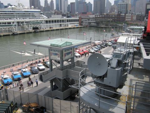 1991 Ford LTD Crown Victoria - Elevated view over the Intrepid museum pier showing classic cars lined up below a naval radar-guided gun mount, with the Manhattan skyline…